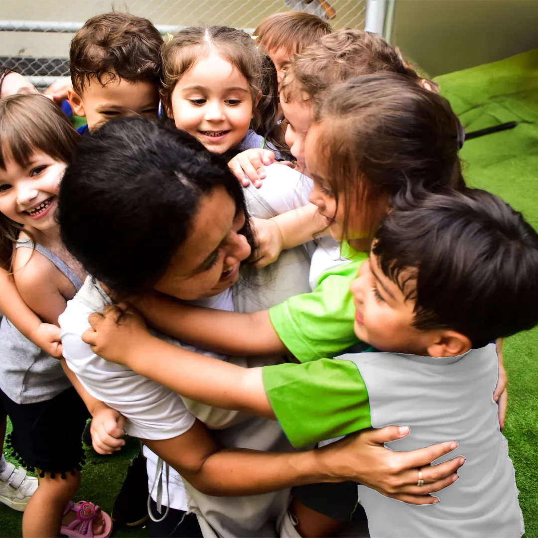 Crianças da Educação Infantil do ZH+ abraçando a professora no pátio da escola